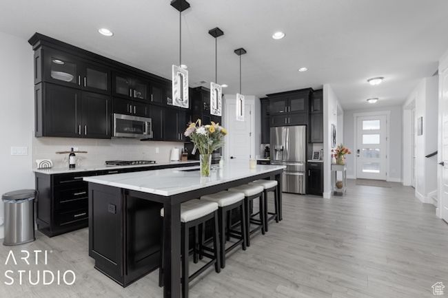 Kitchen featuring a breakfast bar area, stainless steel appliances, a large island, glass insert cabinets, and dark cabinets | Image 11