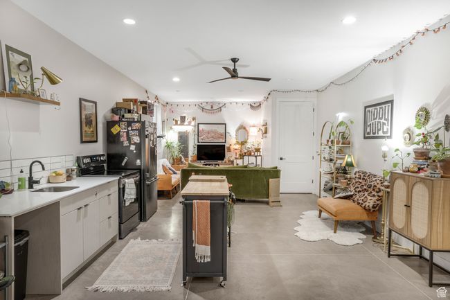 Kitchen with finished concrete flooring, light countertops, electric range, ceiling fan, and a sink | Image 41
