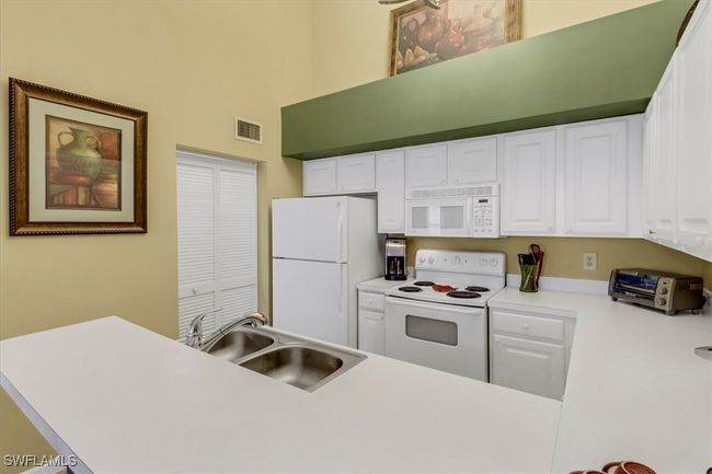 Kitchen with white appliances, white cabinetry, light countertops, and a high ceiling | Image 9