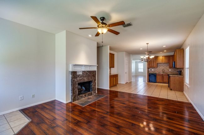 Living room featuring visible vents, baseboards, ceiling fan with notable chandelier, light wood-style flooring, and a premium fireplace | Image 5