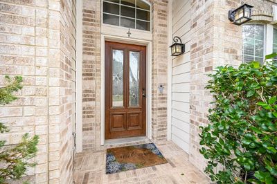 Welcoming entryway featuring a wood-stained door with glass accents, flanked by classic wall lanterns, and framed by an elegant brick exterior. | Image 3