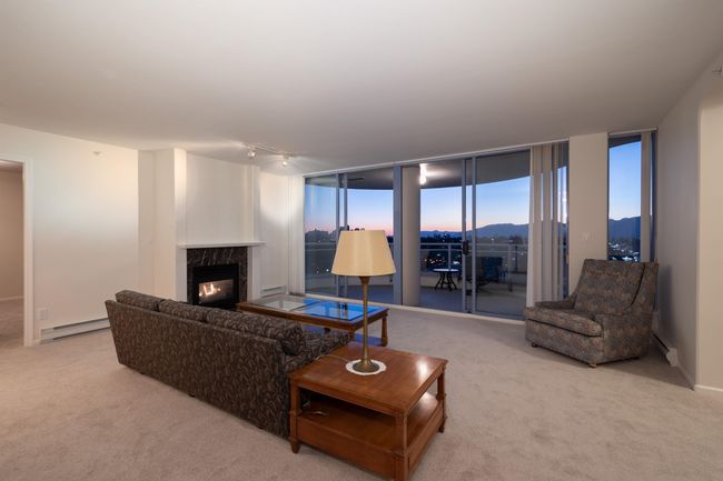 Carpeted living room featuring expansive windows, a high end fireplace, rail lighting, and a baseboard heating unit | Image 4
