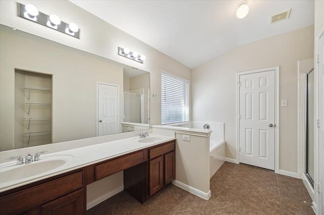 Soak your cares away in the inviting garden tub or refresh in the separate standing shower—now upgraded with a sleek, frosted-new glass door for that modern touch. This spacious en-suite bath offers a blend of relaxation and functionality, complete with dual vanities, neutral tones from new interior paint, and plenty of natural light. Your personal spa retreat awaits! | Image 16