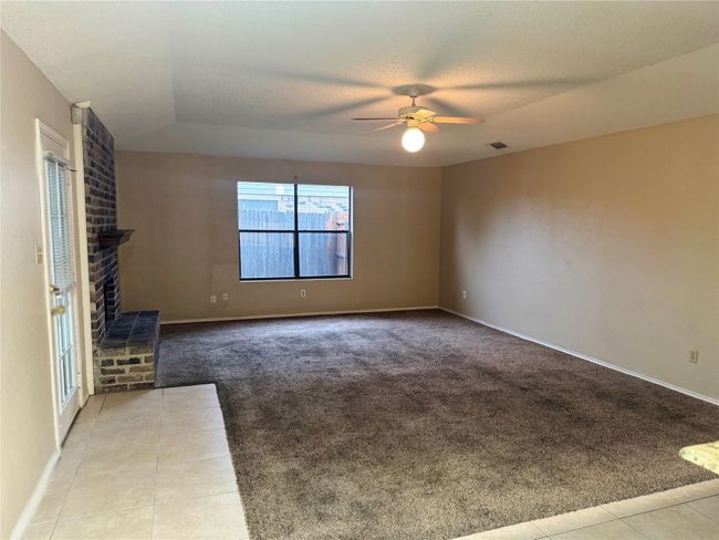 Unfurnished living room featuring light tile patterned flooring, visible vents, a fireplace, ceiling fan, and light carpet | Image 9