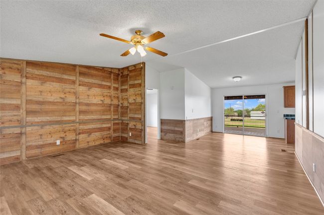 Unfurnished living room featuring ceiling fan, wooden walls, vaulted ceiling, light wood-style flooring, and wainscoting | Image 7