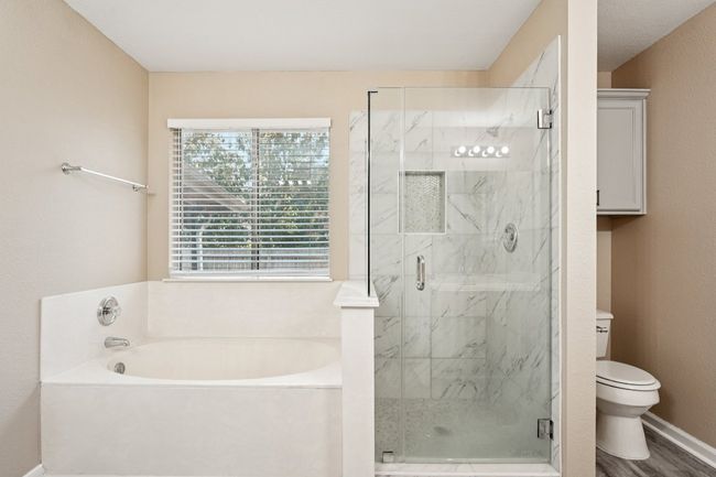 Full bathroom with a bath, a marble finish shower, and a textured wall | Image 23