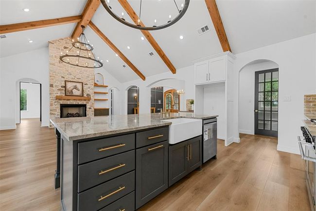 Kitchen featuring high vaulted ceiling, white cabinetry, beam ceiling, a kitchen island with sink, and a fireplace | Image 16