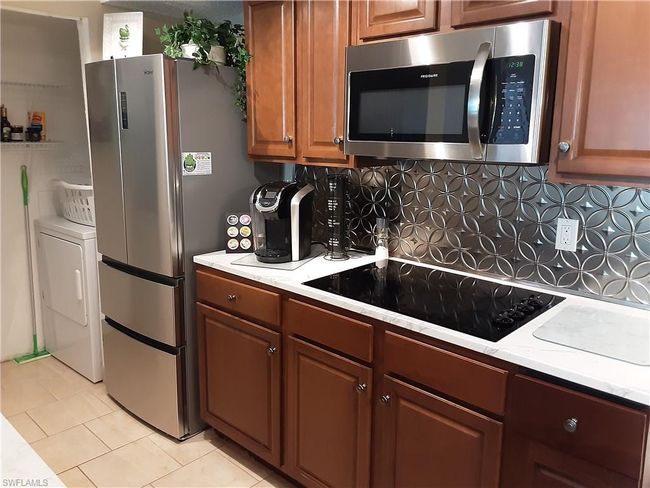 Kitchen with brown cabinets, stainless steel appliances, backsplash, light tile patterned floors, and washer / dryer | Image 10