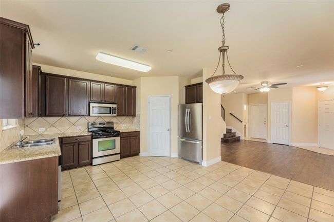 Kitchen featuring stainless steel appliances, open floor plan, dark brown cabinetry, decorative backsplash, and decorative light fixtures | Image 8