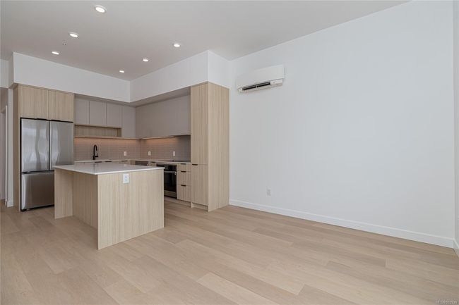 Kitchen with backsplash, a wall unit AC, stainless steel fridge, modern cabinets, and a center island | Image 11
