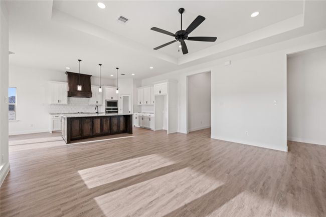 Unfurnished living room featuring a tray ceiling, recessed lighting, a sink, ceiling fan, and light wood-style flooring | Image 13