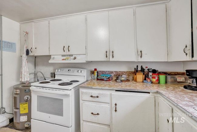 Kitchen featuring electric range, under cabinet range hood, light countertops, white cabinets, and water heater | Image 8