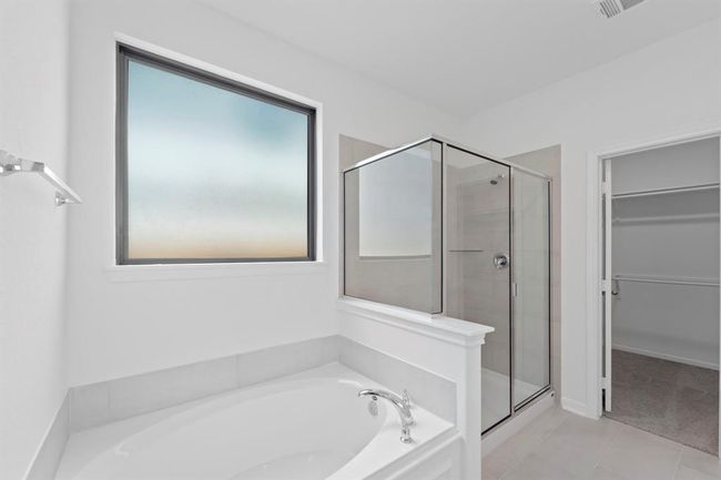 This additional view of your primary bathroom features tile flooring, fresh paint, walk-in shower, a separate garden tub, and a large walk-in closet. | Image 13