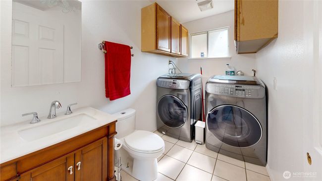 Hall bath combined with laundry space with well-lit by a window that brings in natural light, and the white tile flooring enhances the fresh, clean feel of the space | Image 12
