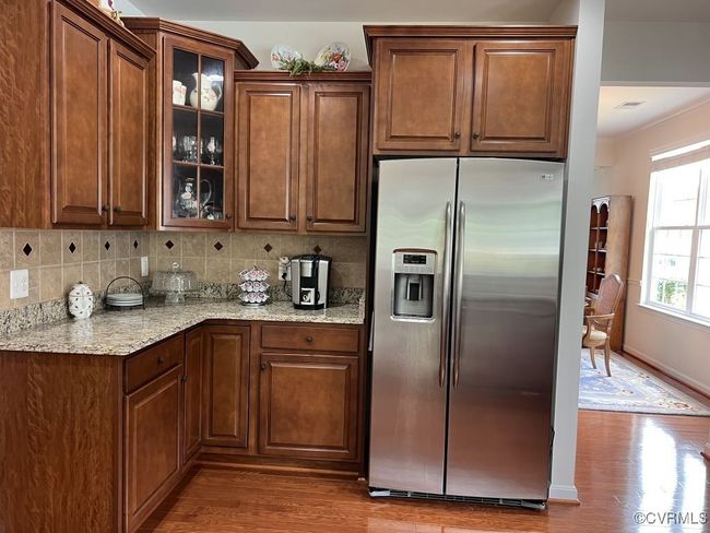 Kitchen featuring backsplash, light stone countertops, stainless steel fridge with ice dispenser, and hardwood / wood-style flooring | Image 21
