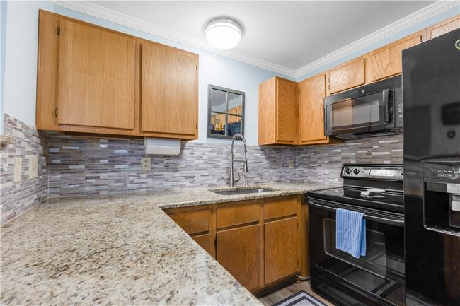 Kitchen with black appliances, tasteful backsplash, ornamental molding, and light stone countertops | Image 6