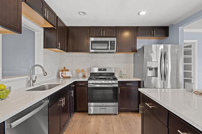Kitchen with dark brown cabinetry, light wood finished floors, appliances with stainless steel finishes, and a sink | Image 12