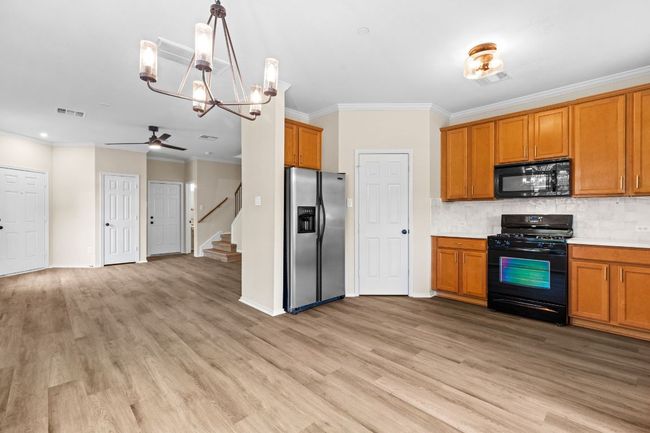 Kitchen featuring brown cabinets, ceiling fan with notable chandelier, ornamental molding, and black appliances | Image 14