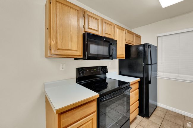 Kitchen featuring black appliances, light brown cabinets, light countertops, and light tile patterned flooring | Image 11