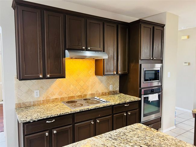 Kitchen with light stone countertops, appliances with stainless steel finishes, light tile patterned floors, and backsplash | Image 10