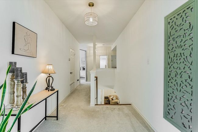 Hallway featuring light colored carpet, an upstairs landing, baseboards, and a chandelier | Image 15