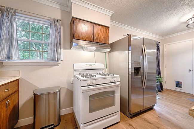 Kitchen with gas range oven, under cabinet range hood, stainless steel fridge, stained wood cabinetry, decorative lighting in dining area. | Image 8