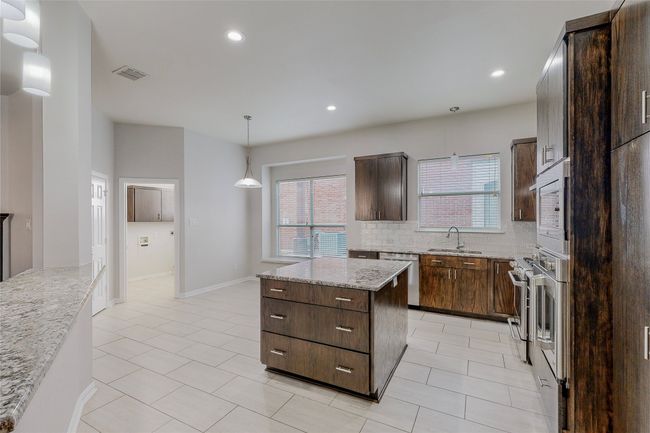 Kitchen with appliances with stainless steel finishes, a kitchen island, decorative backsplash, light tile patterned floors, and dark brown cabinets | Image 17