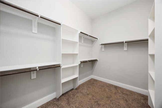 This is a spacious walk-in closet featuring built-in shelves and ample hanging space, with neutral walls and carpet flooring, ideal for organized storage. | Image 25