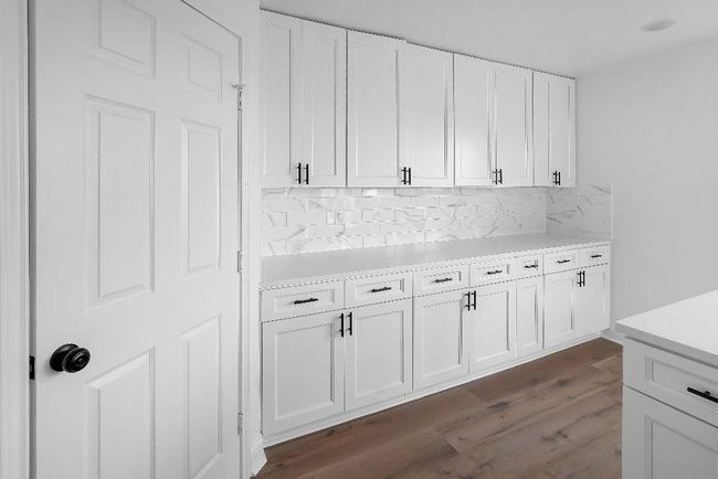 Kitchen with backsplash, light countertops, white cabinets, and dark wood-type flooring | Image 8