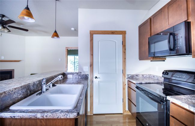 Kitchen featuring black appliances, a ceiling fan, hanging light fixtures, wood finished floors, and a glass covered fireplace | Image 12