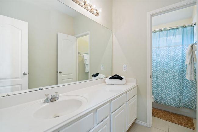 This bathroom features a clean, modern design with a large mirror, ample countertop space, white cabinetry, and a bright blue patterned shower curtain for a pop of color. | Image 36
