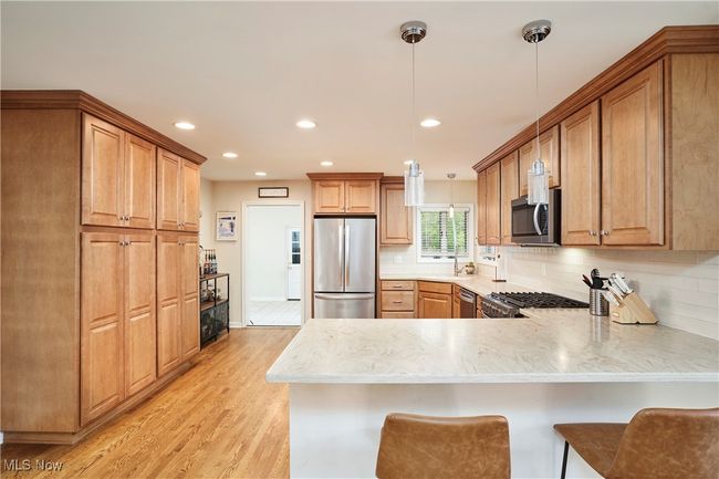 Kitchen featuring appliances with stainless steel finishes, a peninsula, light wood finished floors, backsplash, and recessed lighting | Image 12