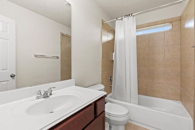 This is a clean, modern bathroom featuring a vanity with a sink, a bathtub with a shower, and neutral tile walls. It's bright and functional, ideal for daily use. | Image 26