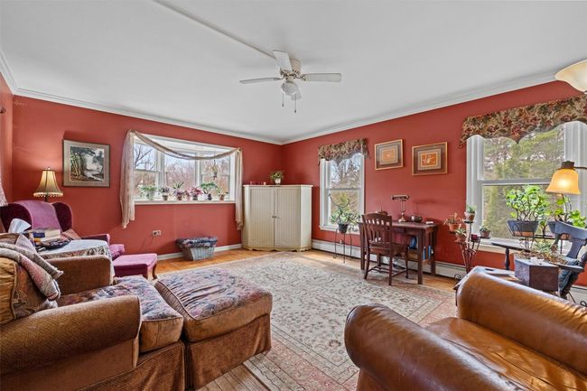 Living area with crown molding, wood finished floors, ceiling fan, and baseboards | Image 11