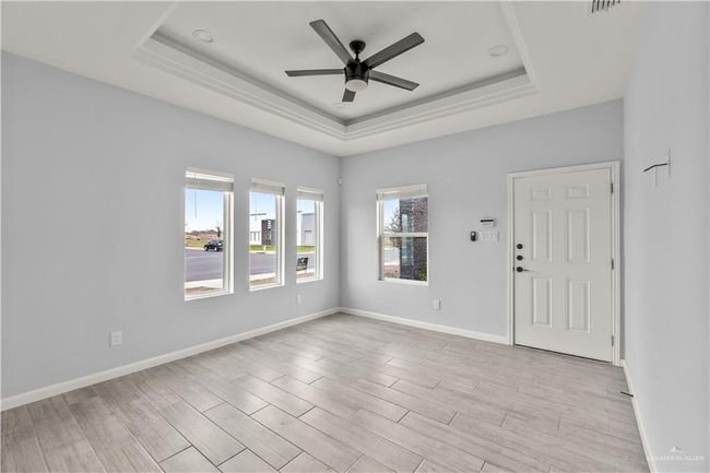 Spare room featuring a raised ceiling, ceiling fan, light wood-style floors, and baseboards | Image 14