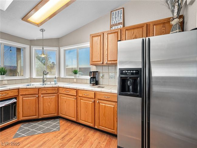 Kitchen with backsplash, tile countertops, light wood-type flooring, stainless steel fridge, and a sink | Image 23