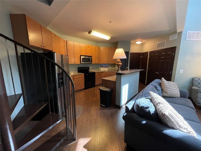 Kitchen featuring black range with electric stovetop, stainless steel microwave, open floor plan, dark wood-type flooring, and brown cabinets | Image 8