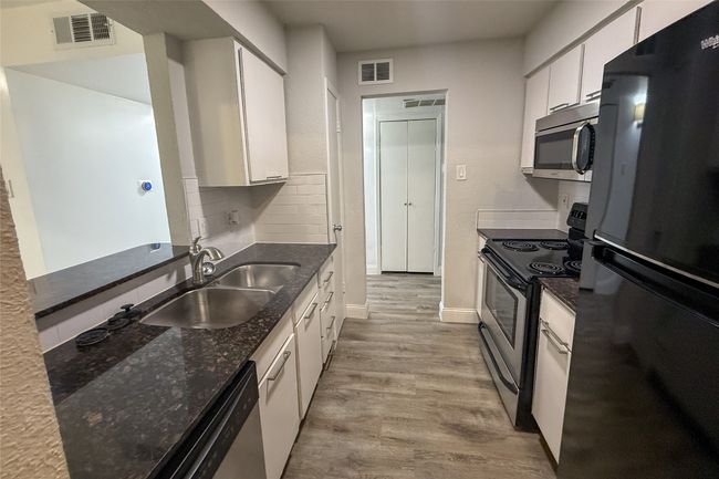 Kitchen with stainless steel appliances, white cabinets, light wood-style flooring, backsplash, and dark stone countertops | Image 15