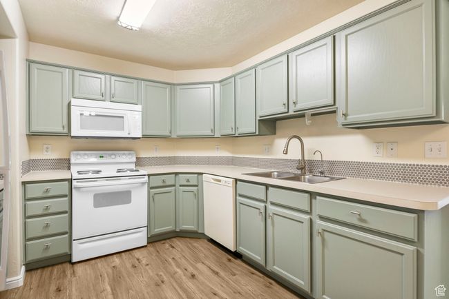 Kitchen featuring white appliances, a sink, green cabinets, light wood-style flooring, and light countertops | Image 7