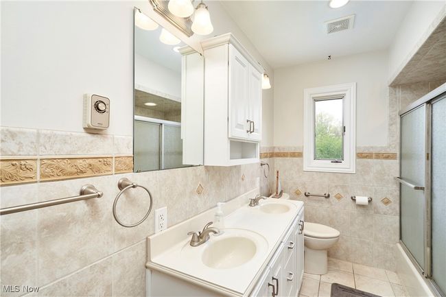 Bathroom with tile walls, tile patterned flooring, double vanity, toilet, and wainscoting | Image 19