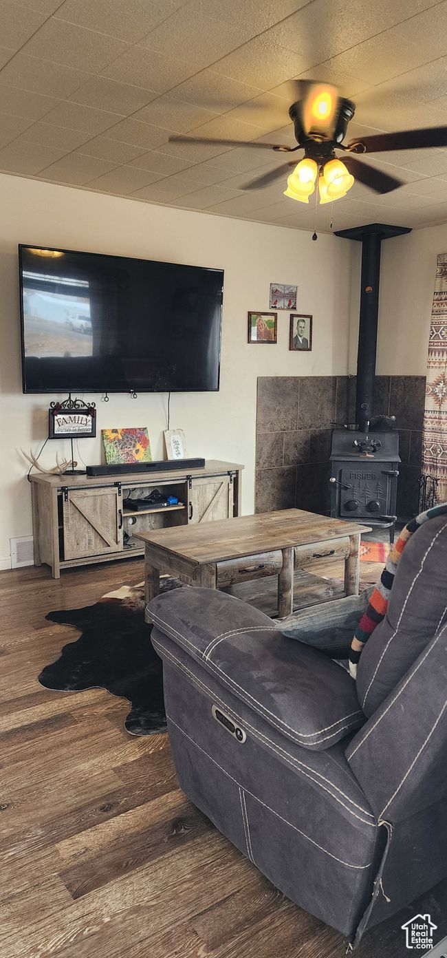 Living room with a ceiling fan, a wood stove, visible vents, and wood finished floors | Image 7
