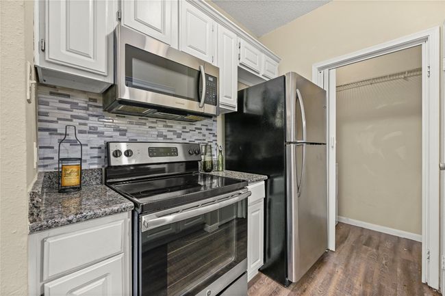 Kitchen with appliances with stainless steel finishes, decorative backsplash, white cabinetry, dark wood-style flooring, and a textured ceiling | Image 9