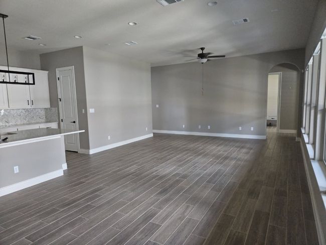 Unfurnished living room featuring a ceiling fan, dark wood-type flooring, arched walkways, and recessed lighting | Image 7