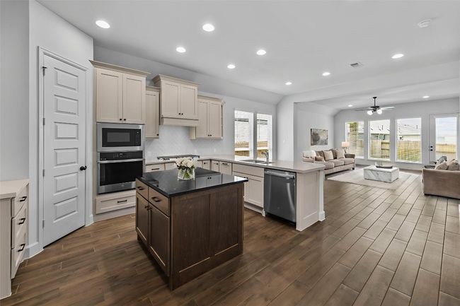 Kitchen featuring open floor plan, stainless steel appliances, dark wood-style floors, a peninsula, and a kitchen island | Image 7