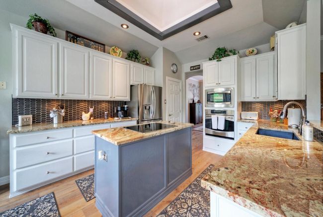 Kitchen featuring a sink, visible vents, white cabinetry, a kitchen island, and appliances with stainless steel finishes | Image 11