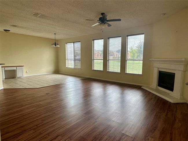 Unfurnished living room with wood finished floors, ceiling fan, a textured ceiling, and a fireplace with raised hearth | Image 5