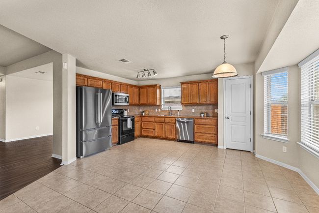 Kitchen featuring stainless steel appliances, light tile patterned flooring, decorative backsplash, decorative light fixtures, and brown cabinetry | Image 20
