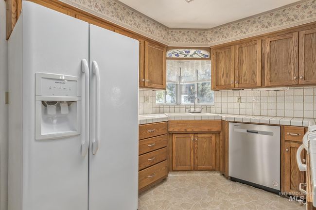 Kitchen with white fridge with ice dispenser, stainless steel dishwasher, brown cabinets, and backsplash | Image 9