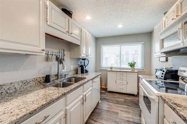 Kitchen with white appliances, a sink, wood finished floors, a textured ceiling, and white cabinets | Image 11