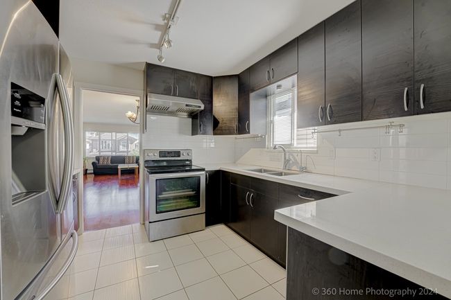 Kitchen featuring a sink, under cabinet range hood, rail lighting, backsplash, and appliances with stainless steel finishes | Image 4